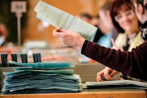 Eine Frau legt einen Stimmzettel auf einen Stapel Wahlunterlagen.